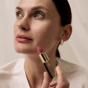 Der Lippenstift auf dem Modell blickt nach oben, während er die geöffnete Tube hält